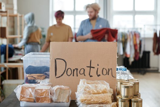 pexels-photo-6994982-6994982 Volunteers sort clothes and food in a donation center. Cardboard sign reads 'Donation.'